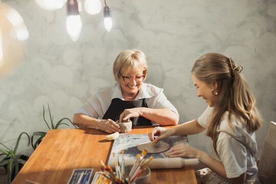 Senior woman and young apprentice creating pottery together in workshop - Powered by Adobe