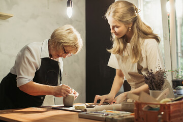 Fototapeta premium Senior woman learning pottery with young artisan in workshop