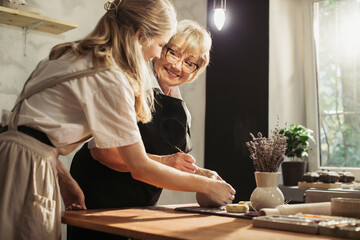 Potter teaching clay modelling to senior woman apprentice in workshop