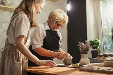 Senior woman learning pottery with teacher in workshop