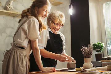 Senior woman and young apprentice sculpting clay together in pottery workshop