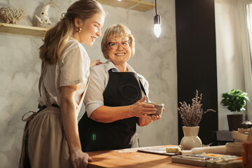 Senior woman learning pottery with young apprentice in workshop