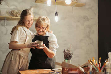Senior woman learning pottery with teacher holding a clay pot