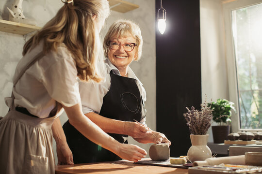 Senior woman enjoying pottery class with teacher - Powered by Adobe