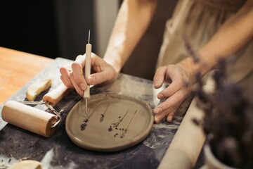 Potter creating lavender design on clay plate in workshop