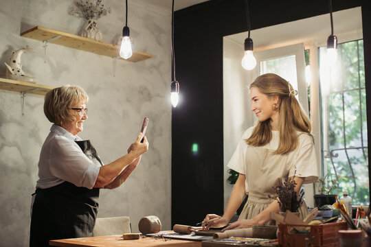 Senior woman taking pictures of young potter working in workshop - Powered by Adobe