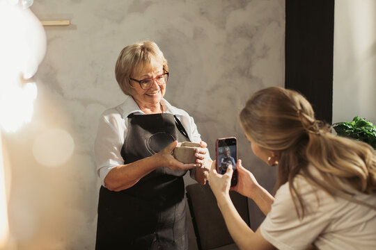 Potter showing handmade clay vase while student is taking photos in workshop