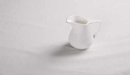 A small white milk jug stands on a white tablecloth