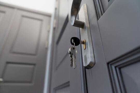 close up of modern apartment door with key in lock, secure entrance with silver handle and dark panel design, real estate access safety and home security concept in residential building interior
