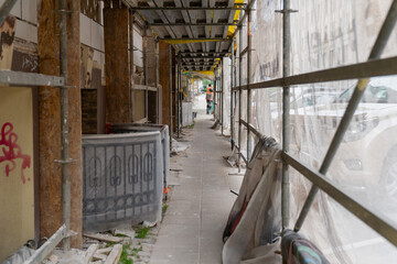 urban sidewalk construction tunnel covered with scaffolding and plastic sheeting protecting...