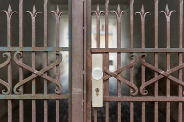 close up of old rusty wrought iron gate with vintage decorative design and white door lock in urban...