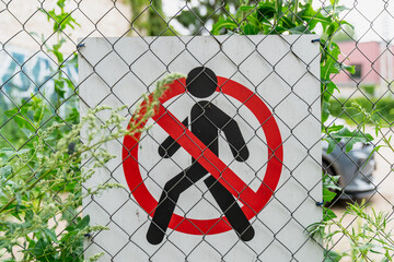 no pedestrians sign on metal fence with green plants and graffiti in background, restricted access...