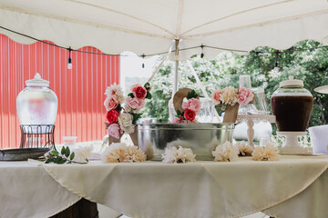 Outdoor wedding beverage station with galvanized ice bucket, decorative floral accents, glass drink...