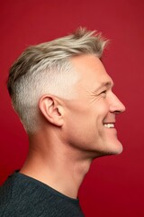 Fototapeta premium Fashionable men's buzz cut haircut - midlife white man with blond hair. Concept of style for aging men. A charming and expressive man enjoying his portrait. Red solid background.