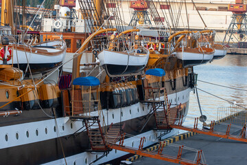 Large classic sailing ship docked in a port with multiple lifeboats suspended and gangways...