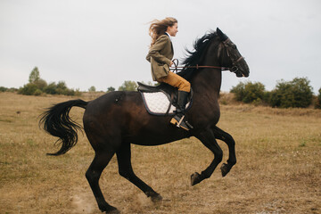 Woman Riding a Black Horse Through an Open Field on a Cloudy Day