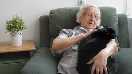 An old lady is petting a black, fat cat