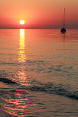 A lone sailboat silhouetted against a breathtaking sunset, with warm hues of orange and red...