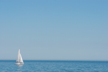 A single white sailboat gracefully glides across the calm, blue expanse of the sea under a clear,...