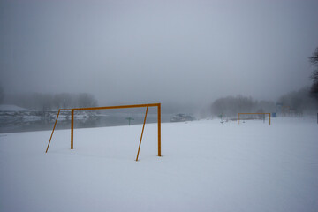 Snow-Covered Field with Yellow Goalposts on a Foggy Winter Day. Desolate Landscape by a Misty River...