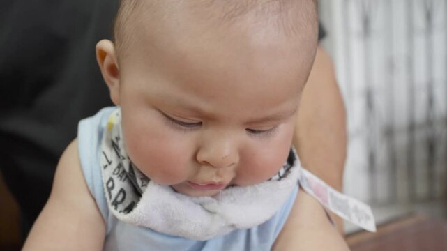 Infant wearing soft bib, drooling and gazing directly at camera with curious, innocent expression capturing pure childhood moment