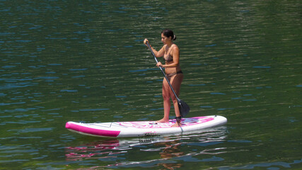 Beautiful brunette woman trains on a stand up paddle board in the lake of Piazze in Trentino,...
