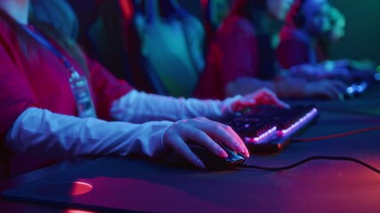Medium closeup of hands and midsection of team of unrecognizable female gamers sitting in front of computers in cyberclub, playing video game with keyboard and mouse