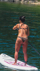 Beautiful black-haired woman in a bikini on a stand up paddle board in the picturesque scenery of...