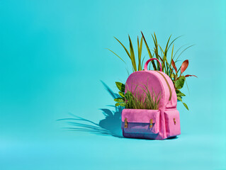 Pink backpack with wild plants growing out of it on a vibrant teal background. Back to school, education neglection conceptual copy space backdrop.