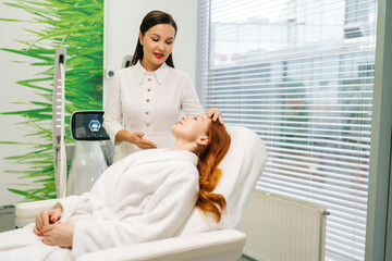 Professional beautician consulting with young woman client lying comfortably on modern bed,...