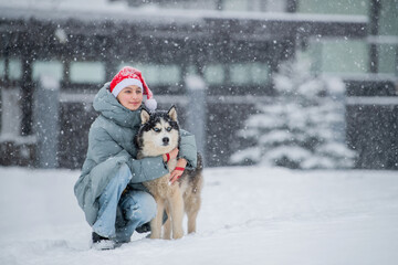 Happy girl owner wearing Santa hat hugging husky dog snowy winter
