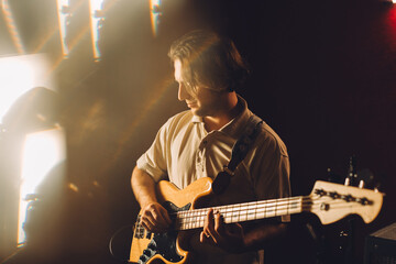 Musician playing bass guitar in recording studio with backlight