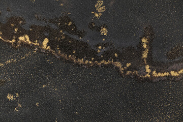 Creating abstract art with black and gold alcohol ink on a textured canvas background