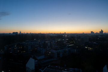 Cologne city skyline at dawn with orange sky and silhouetted city buildings.