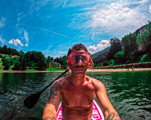 Tourist with swimming mask sitting on a stand up paddle board in the lake of Piazze in Trentino,...