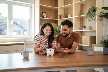Young couple saving money together at home using piggy bank