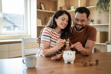 Happy couple saving money together at home putting coins in piggy bank