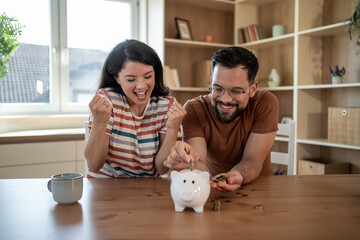 Happy couple saving money at home putting coins in piggy bank