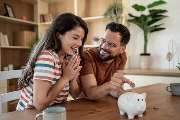 Happy couple saving money together, putting coin in piggy bank at home