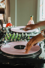 DJ hands scratching pink vinyl records on dual turntables with mixer knobs in a modern home studio...