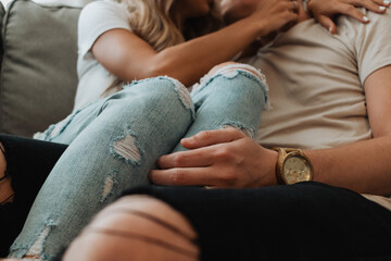 Intimate close-up of a couple cuddling on a couch in ripped jeans showcasing affectionate body...