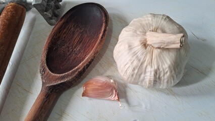 Garlic bulb, clove, wooden spoon and meat tenderizer on a cutting board