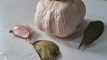Garlic bulb, clove, and bay leaves on a cutting board