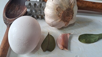 Garlic, clove, and bay leaves on a kitchen surface with cooking tools