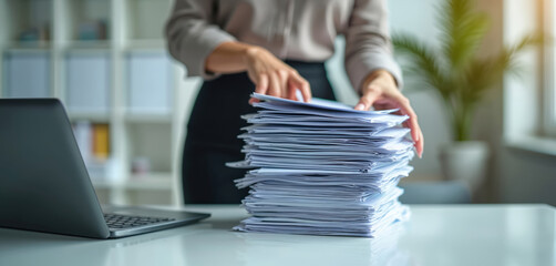 Businesswoman works with documents in office. Woman holds stack of paper near laptop. Employee deals with paperwork. Office routine, bureaucracy. Overwork, document flow, data processing.