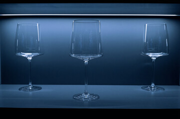 3 modern wine glasses and tableware in tableware cabinet with blue light. Sale of glassware,...