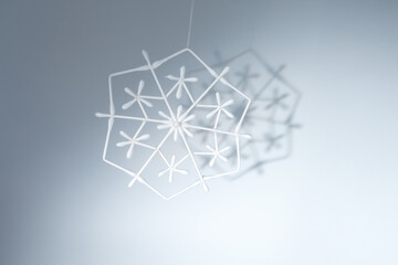 Hanging handmade snowflake decorations made from cotton swabs with shadows on white background. DIY winter ornament project. Christmas and seasonal decor concept, holiday, creative workshops, 