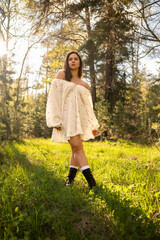 Young woman in a light summer dress standing in a sunny forest clearing