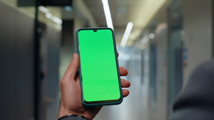 Hands holding mockup mobile phone in office vestibule closeup. Man strolling