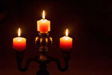 Close-Up of Three Lit Orange Candles on Candle Holder in Darkness